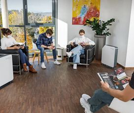 Patienten sitzen zwischen mobilen UV-C Luftentkeimungsgeräten im Wartezimmer einer Arztpraxis